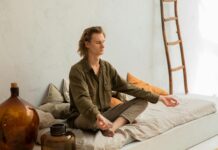 Mindful Movement: Incorporating Yoga and Exercise into Your Wellness Routine concentrated man meditating in lotus pose on mattress